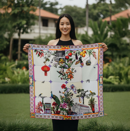 A woman stands outdoors in a garden holding up a large square scarf. 100% silk twill scarf showing hand-rolled edges and Peranakan shophouse, Fullerton Hotel, Super trees, lantern and black and white bungalow