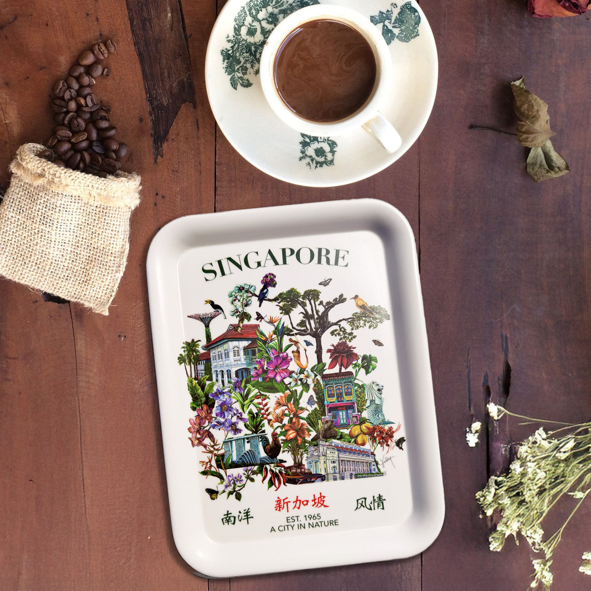 A rectangular bamboo tray with rounded corners, printed with a colorful illustration of Singaporean houses, flowers, birds, and the text 'SINGAPORE' and '南洋风情', is photographed on a dark wooden table. 
